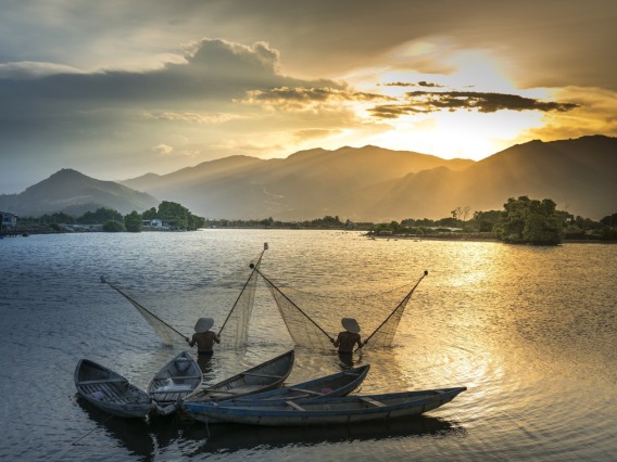 Fishermen in the Mekong River with sun and mountains in the background.
