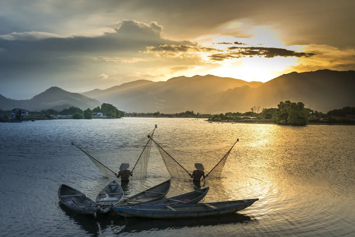 Fishermen in the Mekong River with sun and mountains in the background.