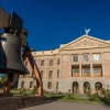 The Arizona liberty bell is in the foreground with the white Arizona state capitol building in the background, with the winged Victory statue atop.