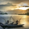 Fishermen in the Mekong River with sun and mountains in the background.